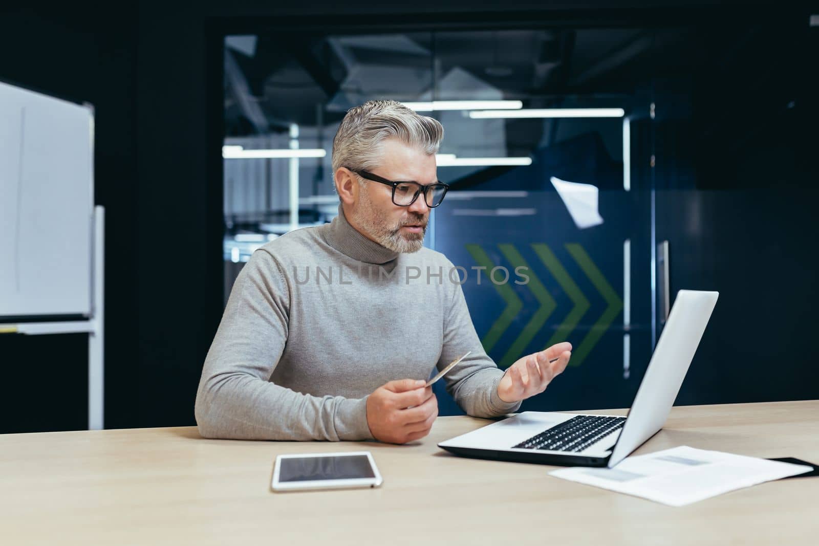 Senior gray haired businessman in office frustrated and sad trying to make bank transaction and purchase in online internet store, man holding bank credit card and using laptop.