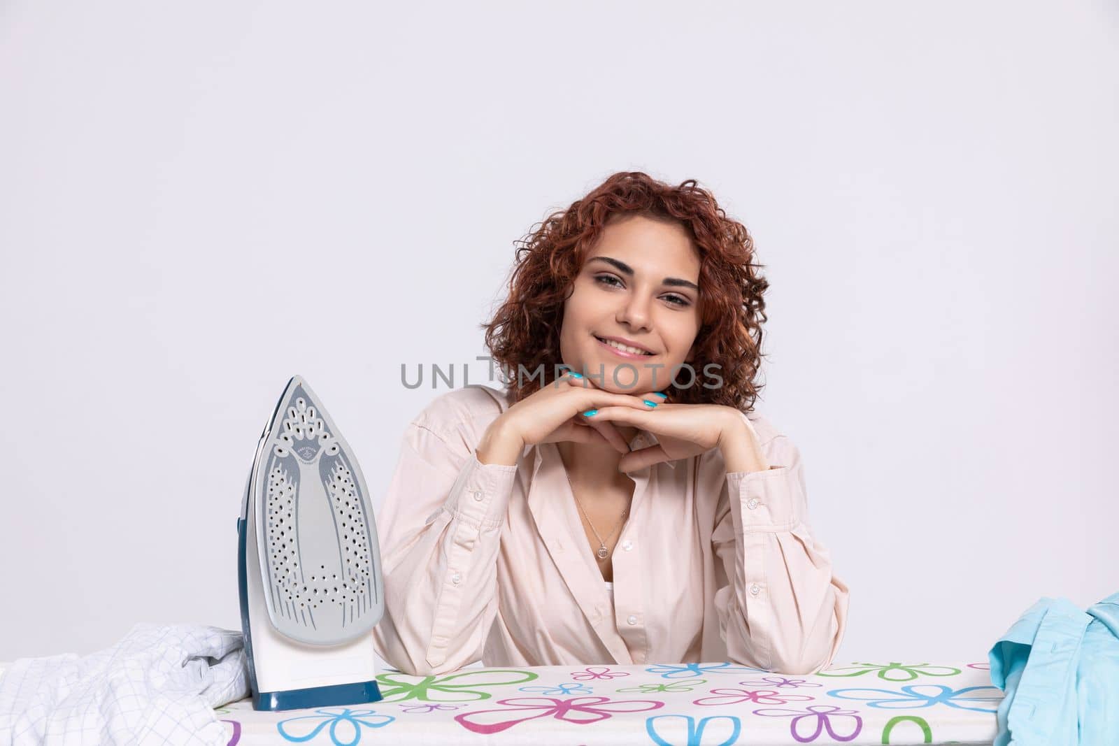 A happy and full of joyful smile girl sits at the ironing board and iron. An eager woman for work.