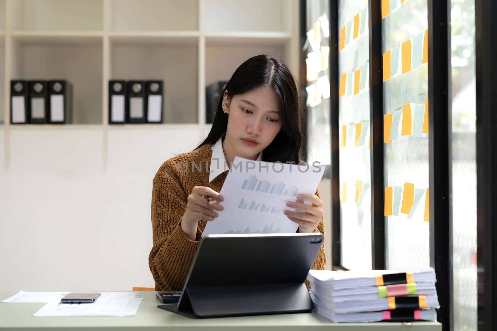 Asian Business woman using calculator and laptop for doing math finance on an office desk, tax, report, accounting, statistics, and analytical research concept by wichayada