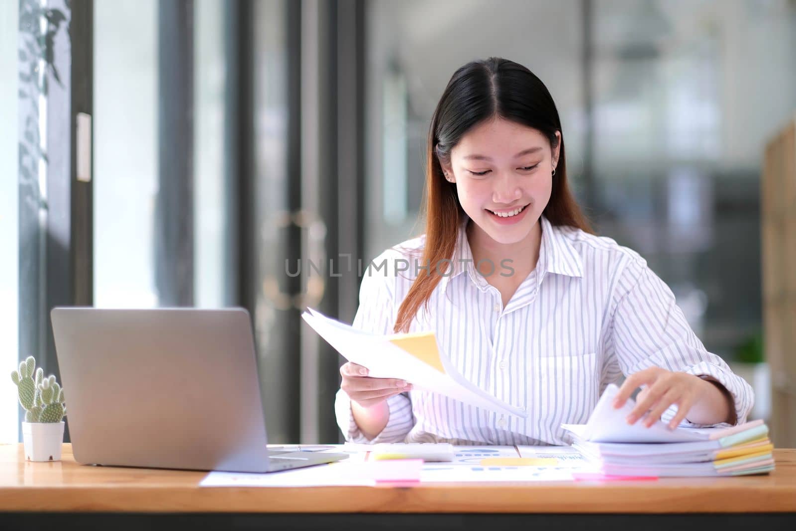 Business Documents concept : Employee woman hands working in Stacks paper files for searching and checking unfinished document achieves on folders papers at busy work desk office. Soft focus by wichayada