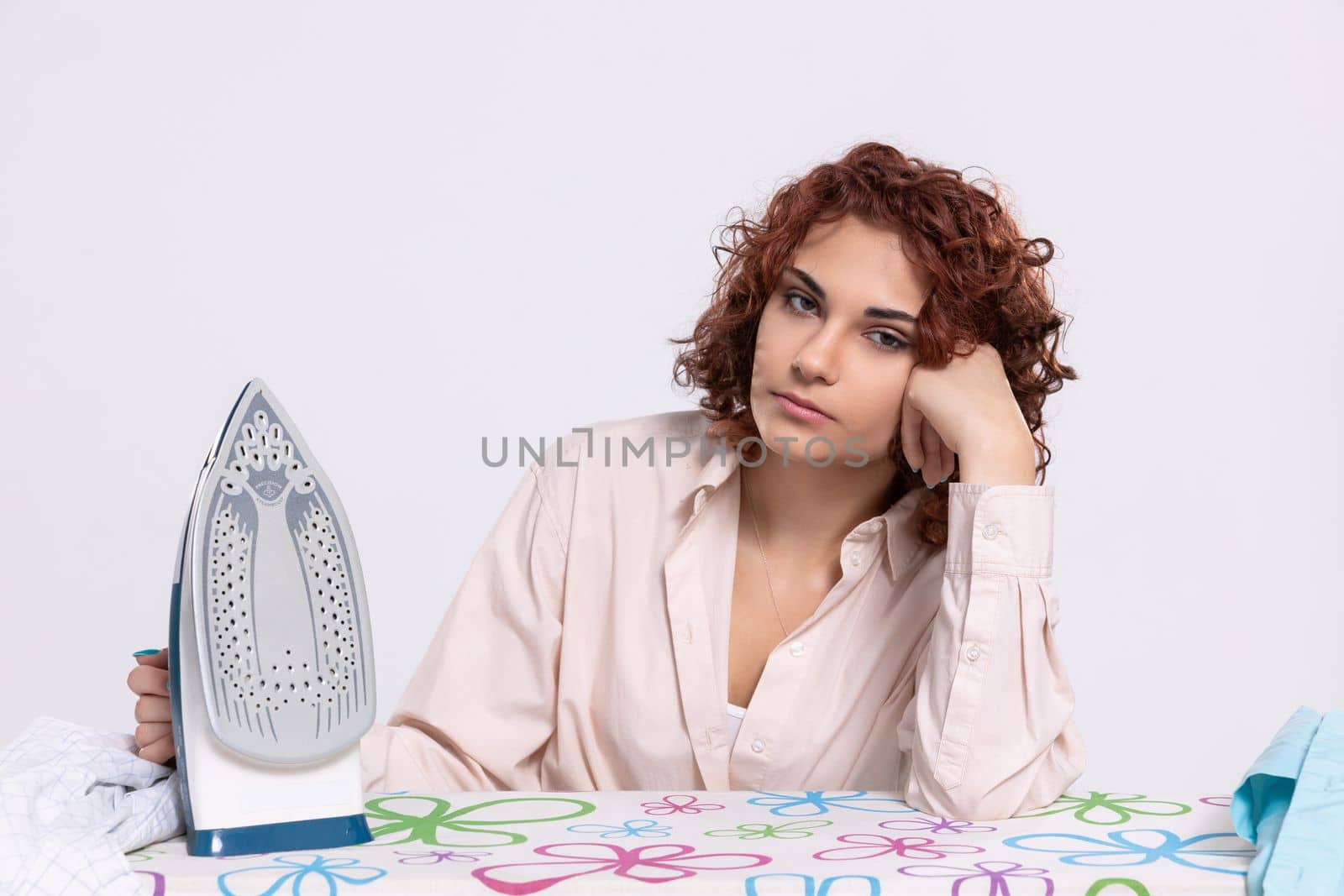 At the ironing board sits a girl, worried and disappointed by the constant ironing of shirts. Monotonous housework.