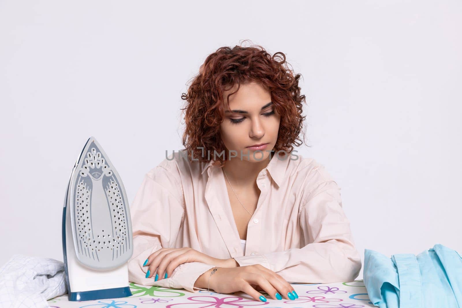 The girl sits at the ironing board, quite tired of this work. Daily housework after washing clothes is ironing shirts.