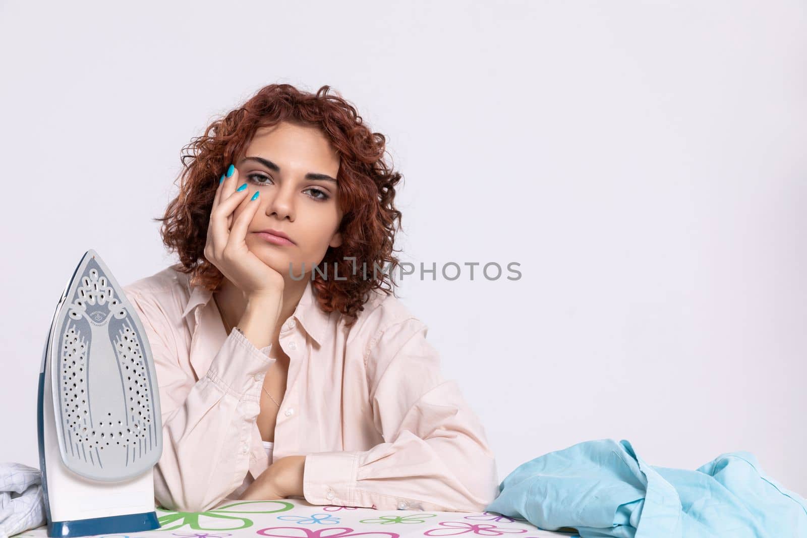 At the ironing board sits a girl, worried and disappointed by the constant ironing of shirts. Monotonous housework.