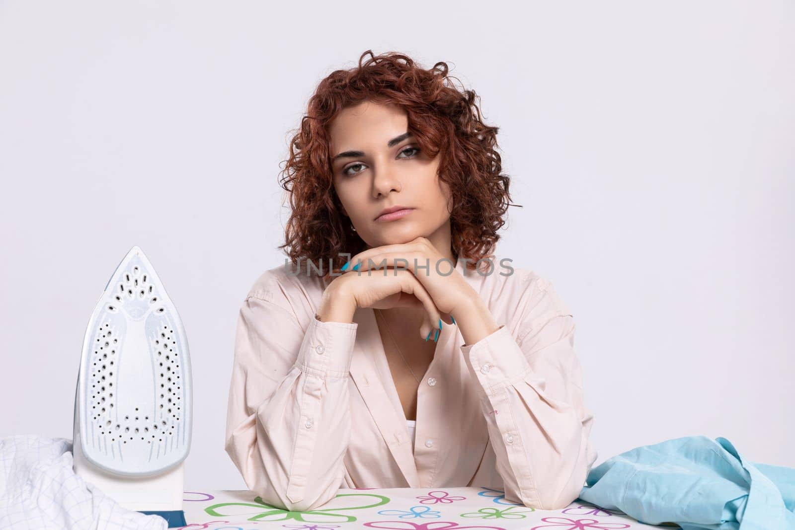 At the ironing board sits a girl, worried and disappointed by the constant ironing of shirts. Monotonous housework.