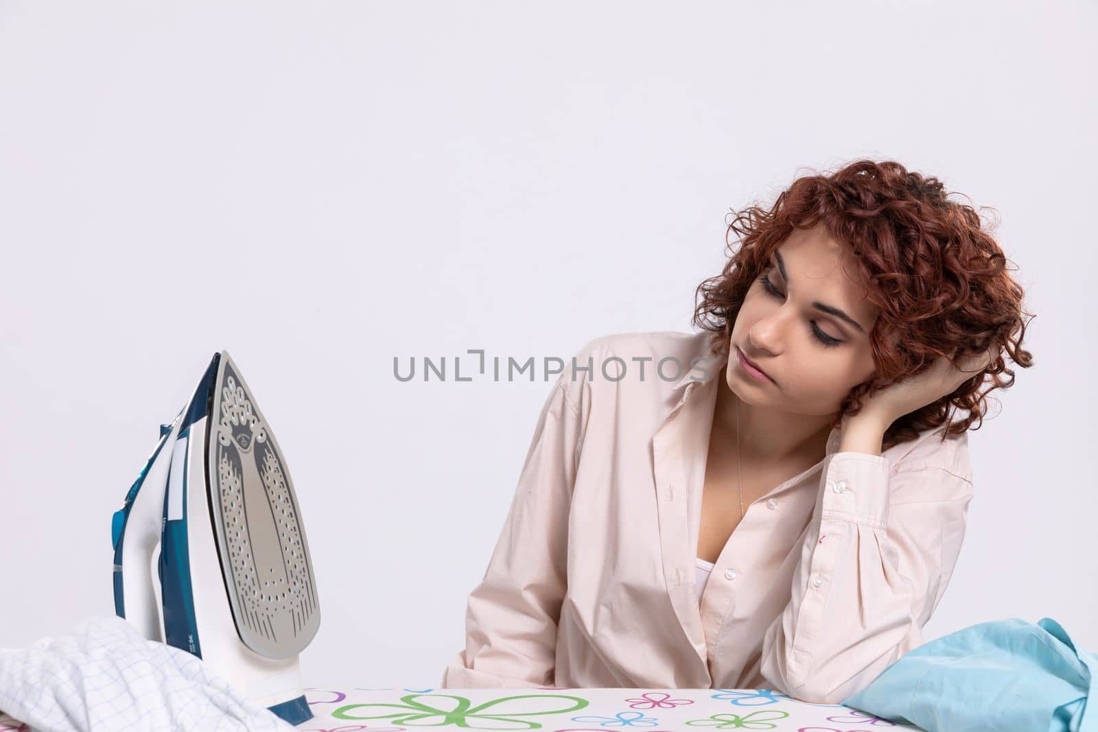 The girl sits at the ironing board, quite tired of this work. Daily housework after washing clothes is ironing shirts.