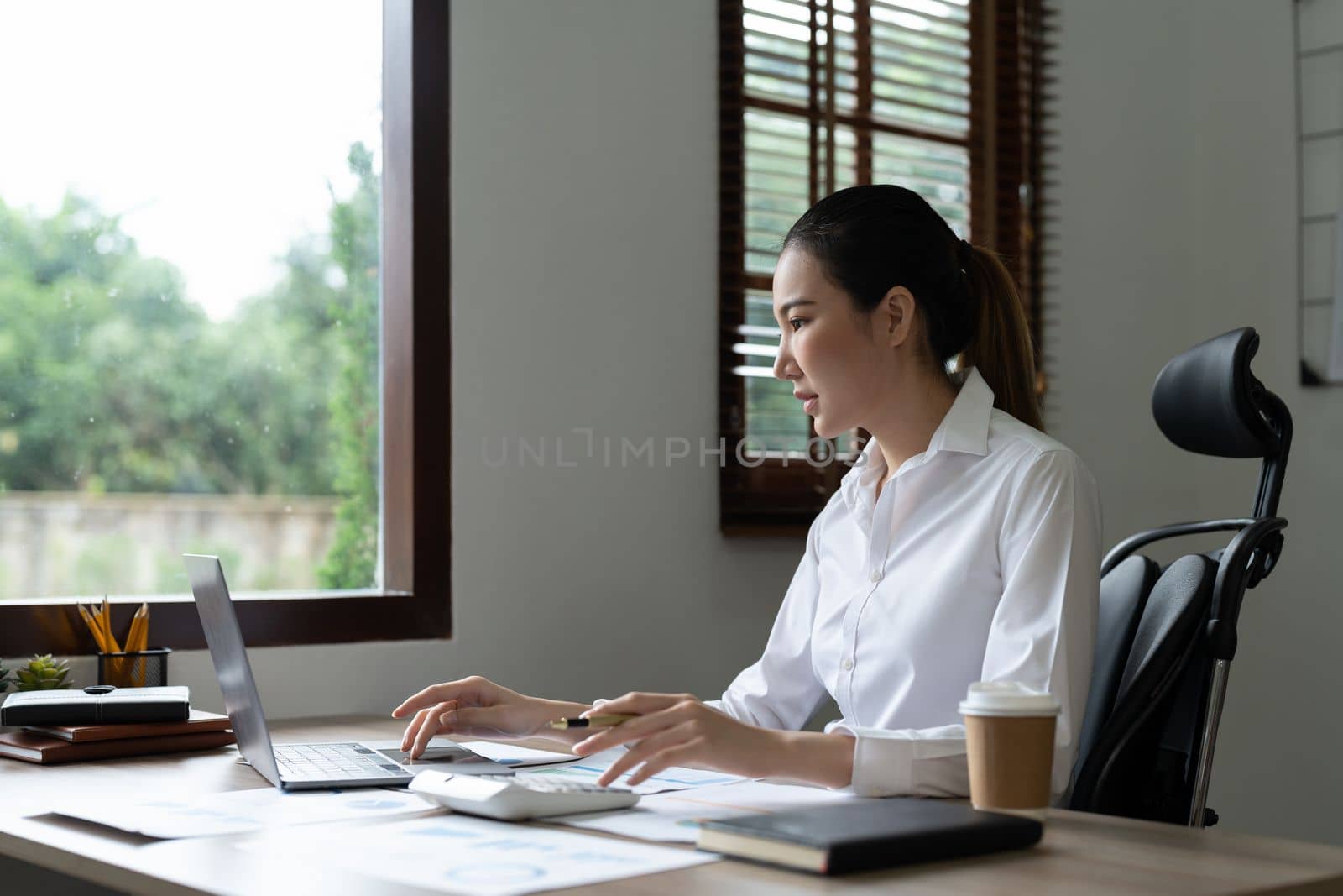 Woman accountant using calculator and laptop computer in office, finance and accounting concept.