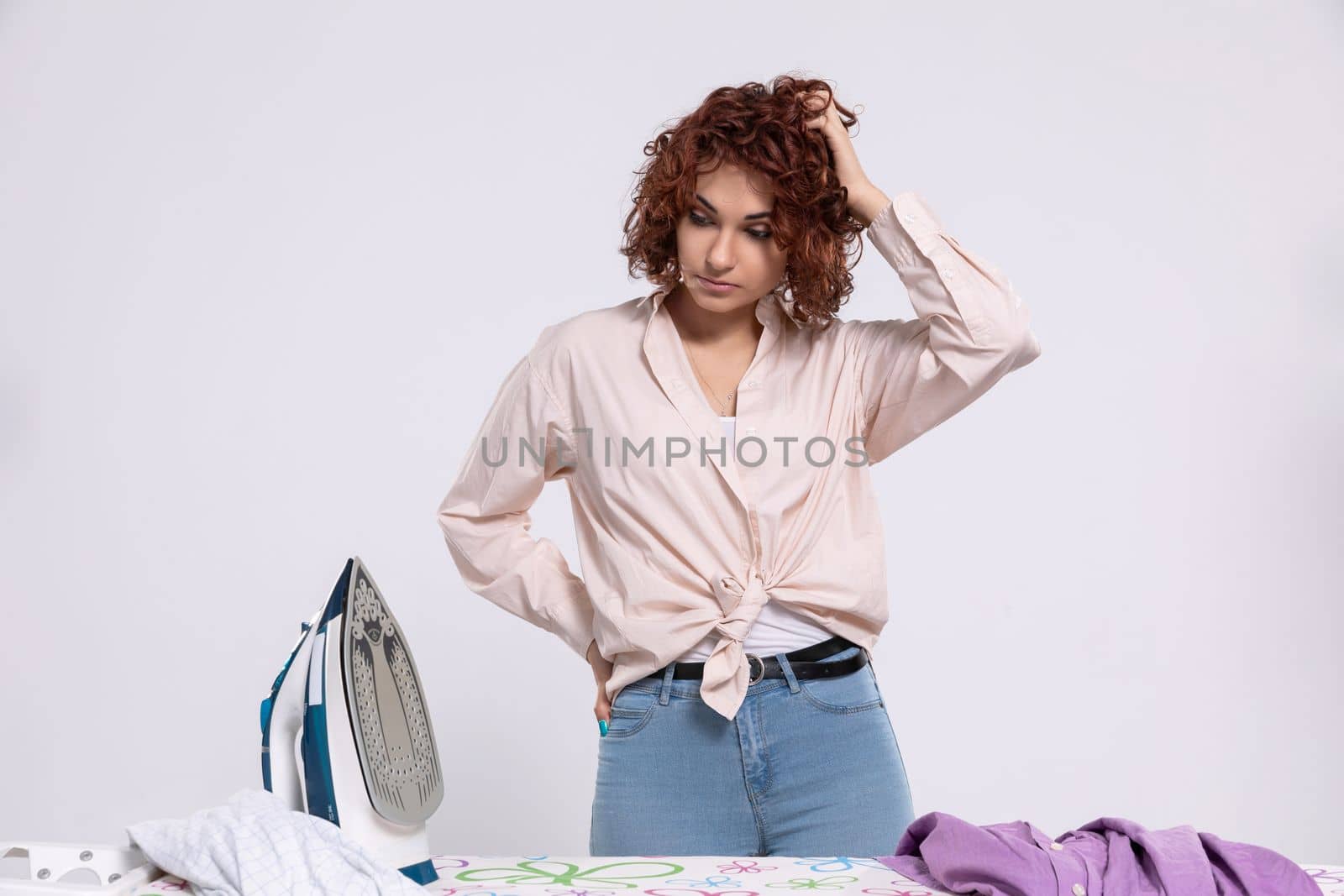 The woman stood over the ironing board and thinks where to start in order to get this job done as quickly as possible. Lots of clothes to iron.
