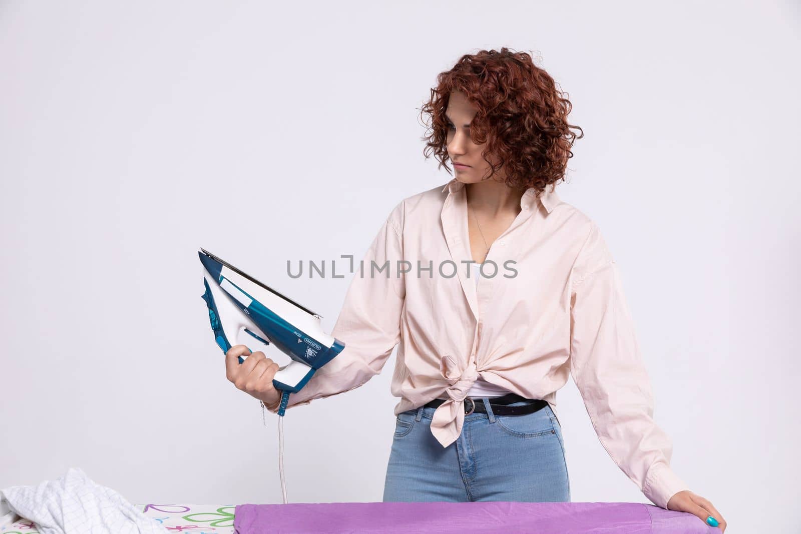 The woman stood over the ironing board and thinks where to start in order to get this job done as quickly as possible. Lots of clothes to iron.