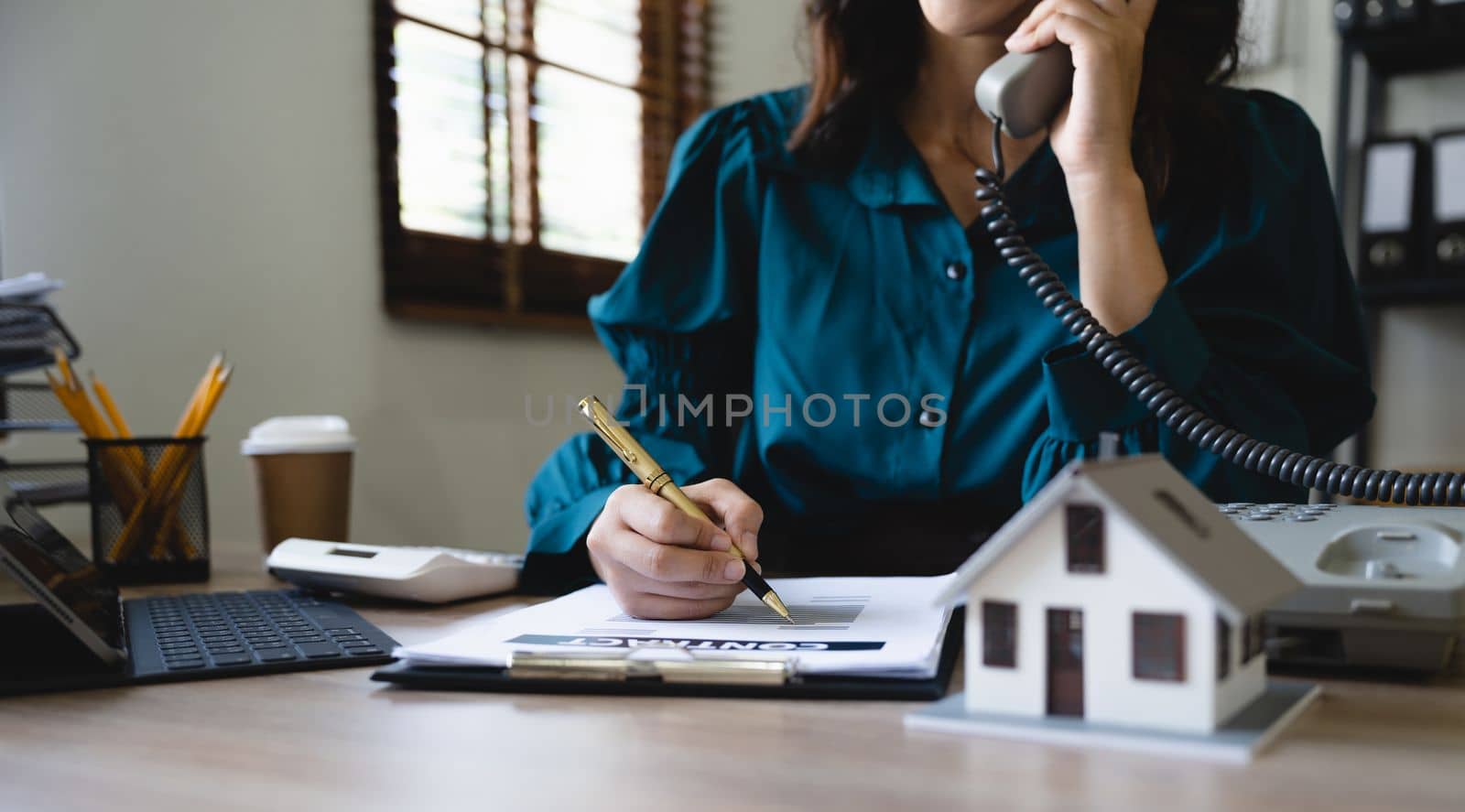 Home loan contract. house model on workplace desk with real estate agent professional making business call talking on phone with customer for signing rental lease contract in office concept.