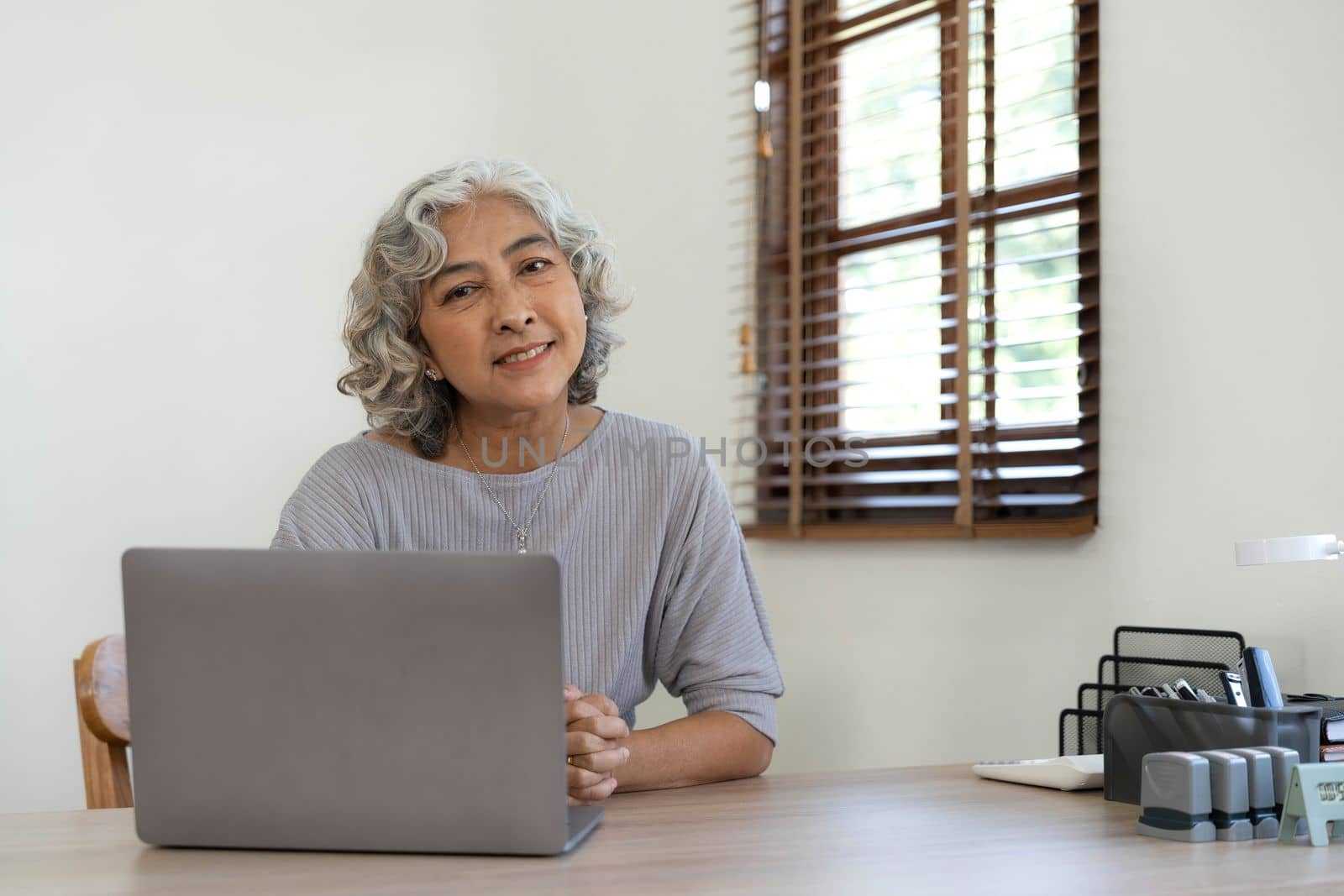 Portrait of smiling asian senior mature middle aged businesswoman using laptop working and web surfing on desk