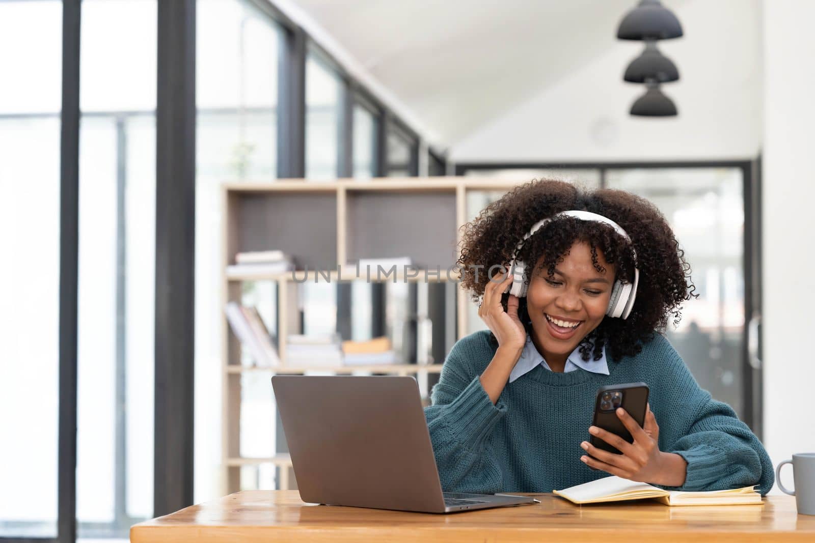 Photo of cheerful joyful mixed race woman playing games and wearing wireless headphones at home Play game on your smartphone that wins the moment of victory. Fun and enjoyable vacation.