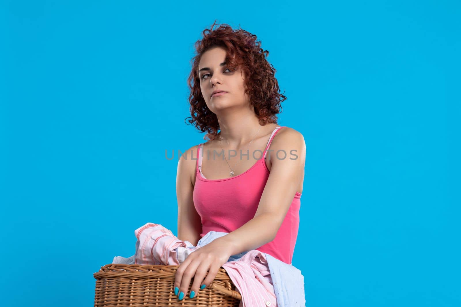 A very tired woman , carries a heavy wicker basket with washed clothes. Overworked woman with dark and curly hair. Monotonous housework.