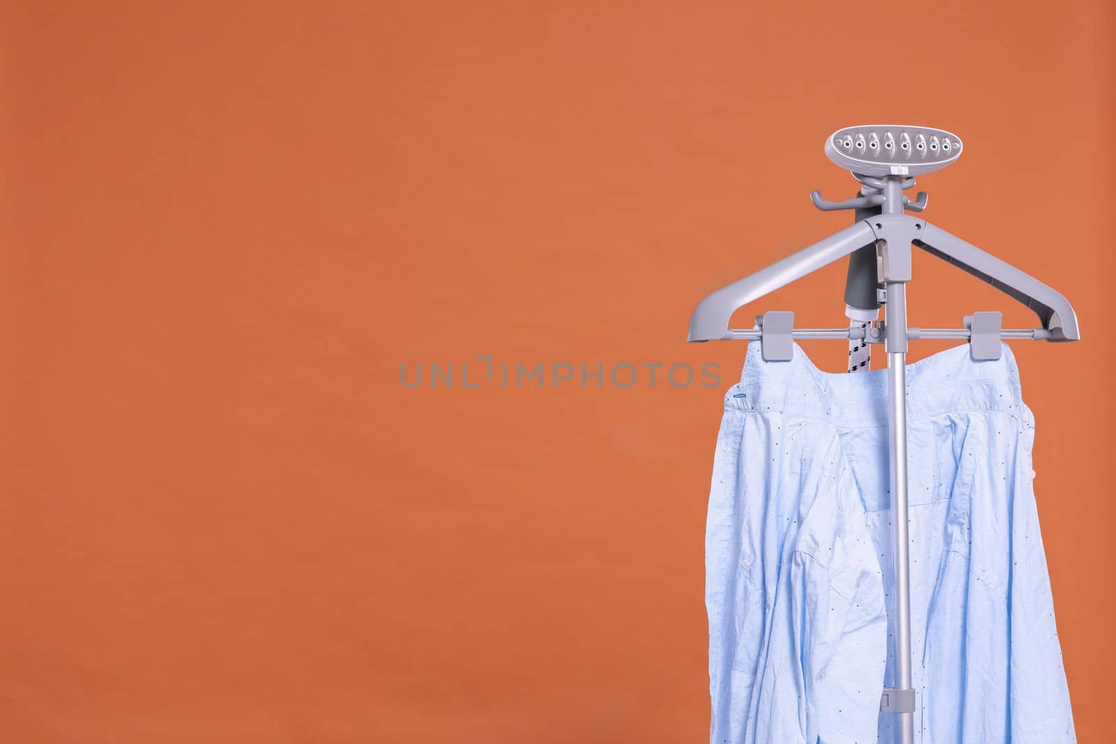 Men's shirt. Hot steam device for ironing clothes with hanger. Uniform brick-colored background. Isolated from the background.