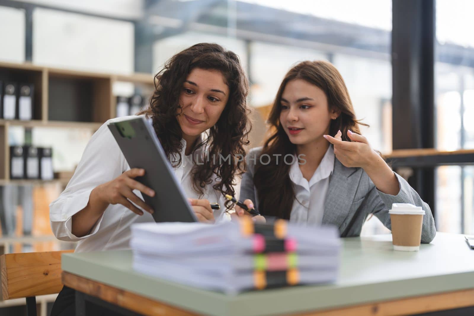Two smart multiethnic business people working together with laptop while talking about job news in the office