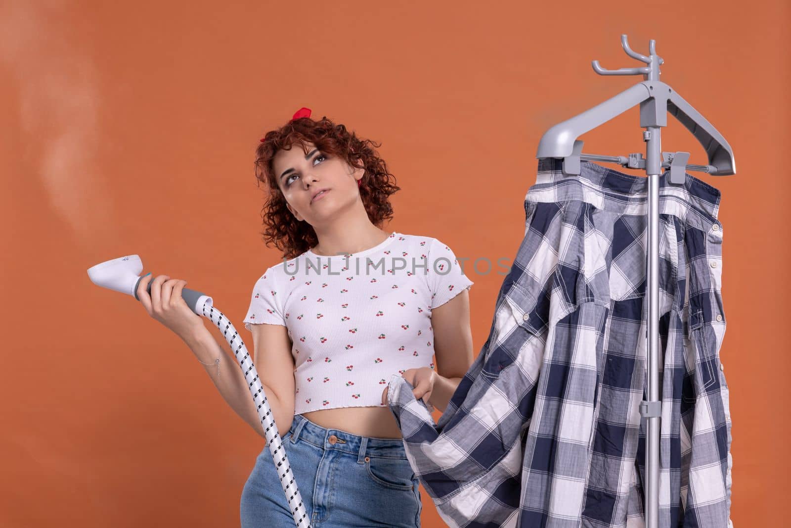 A woman is pondering and bubbling while ironing her shirt. Ironing steamer. Attractive girl with dark and curly hair. Hot steam.