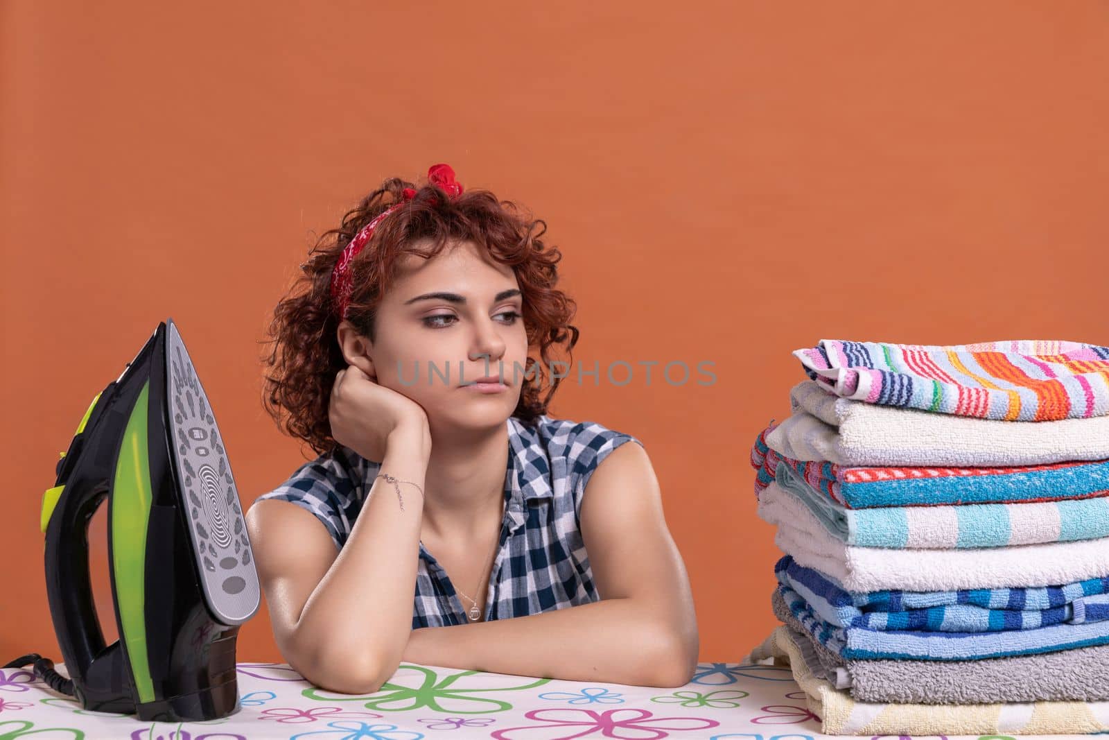 Ironed and folded towels in a fuzz. Tired girl with curly hair. Uniform brick-colored background. Isolated from the background.