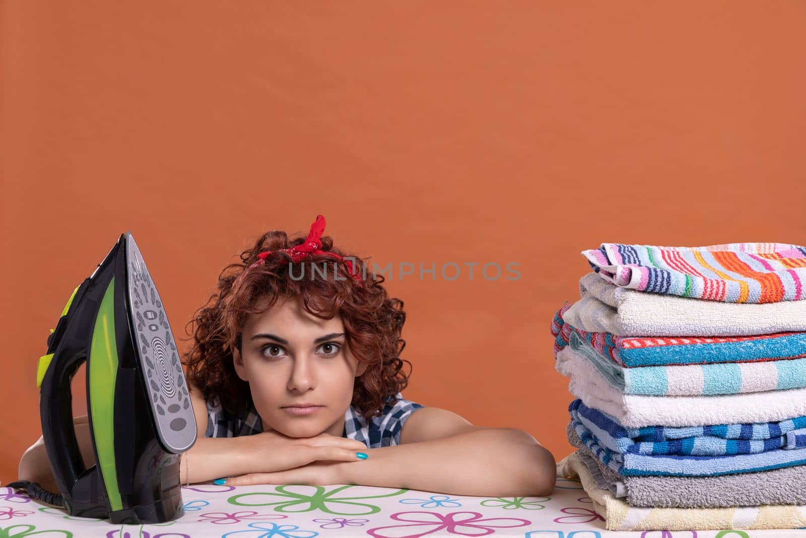 The young woman has ironed all the towels and is now waiting for the next batch. Attractive girl with curly hair. Isolated from the background.