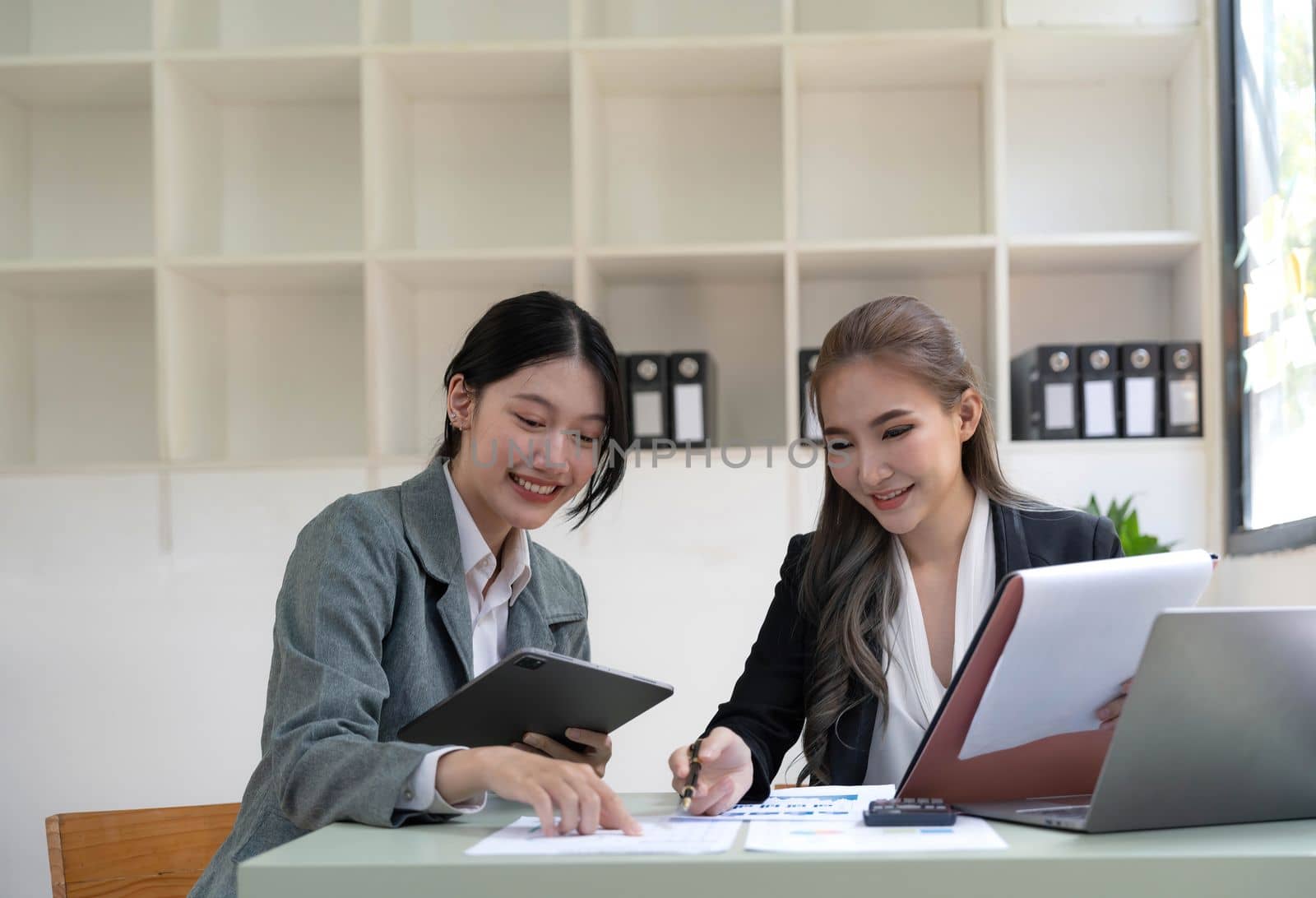 Two young Asian business woman talk, consult, discuss working with new startup project idea presentation analyze plan marketing and investment in the office. by wichayada