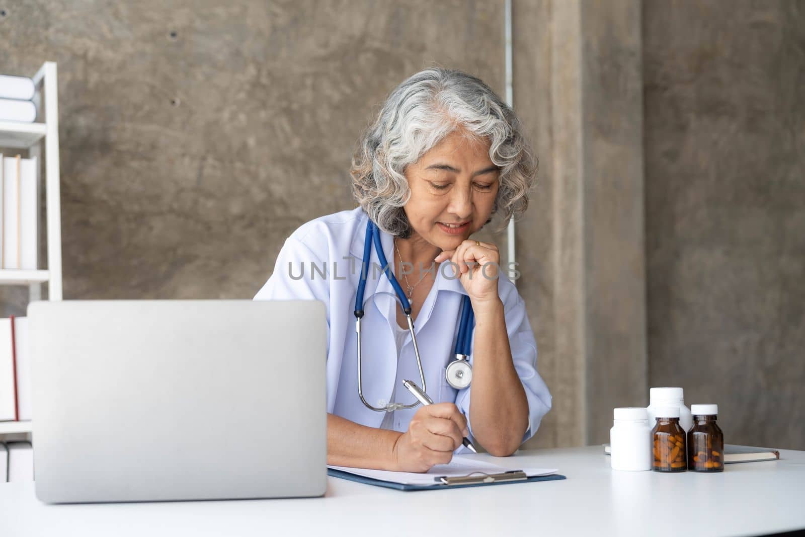 Portrait of senior grey-haired female doctor in her office using laptop for video chat with a patient. Online consultation with doctor for diagnoses and treatment recommendation
