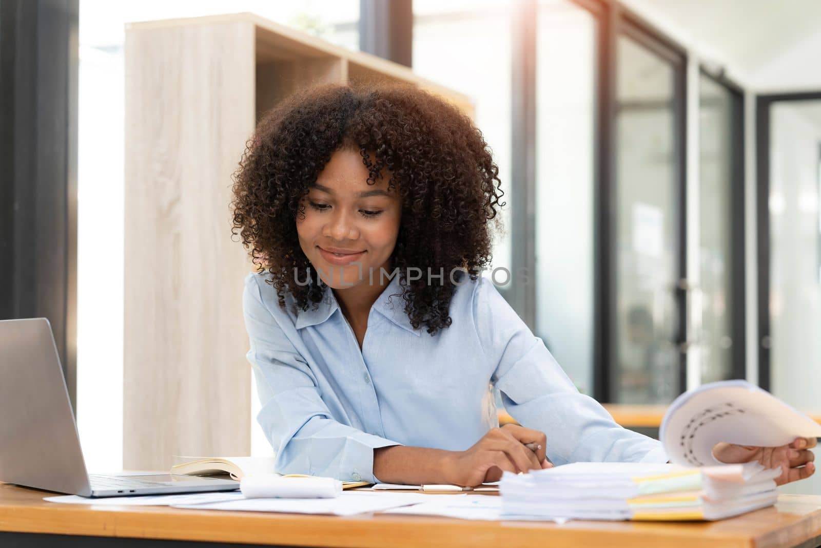 Smiling young African female entrepreneur sitting at a desk in her home office working online with a laptop.