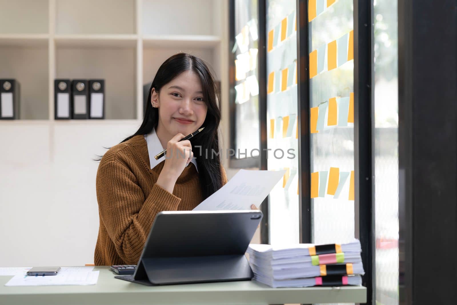 Asian Business woman using calculator and laptop for doing math finance on an office desk, tax, report, accounting, statistics, and analytical research concept..