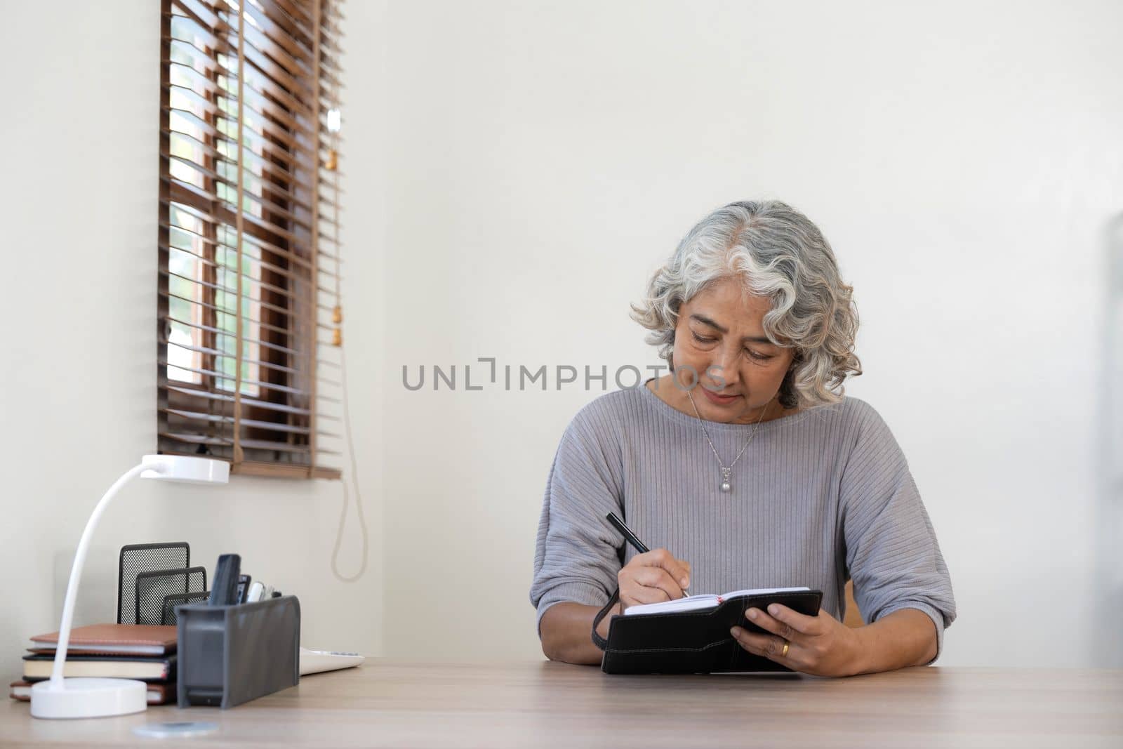 Senior stylish woman taking notes in notebook while using laptop at home