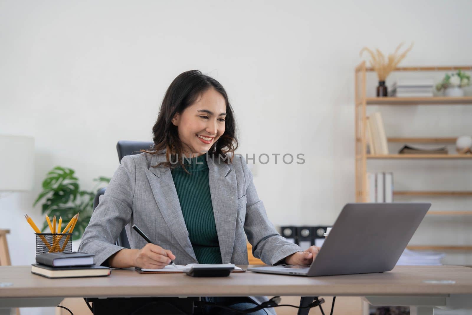 Asian Business woman using calculator and laptop for doing math finance on an office desk, tax, report, accounting, statistics, and analytical research concept..
