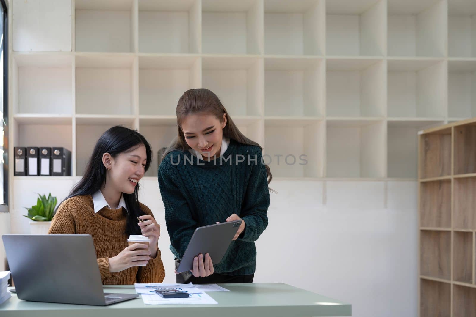 Two young Asian business woman talk, consult, discuss working with new startup project idea presentation analyze plan marketing and investment in the office. by wichayada