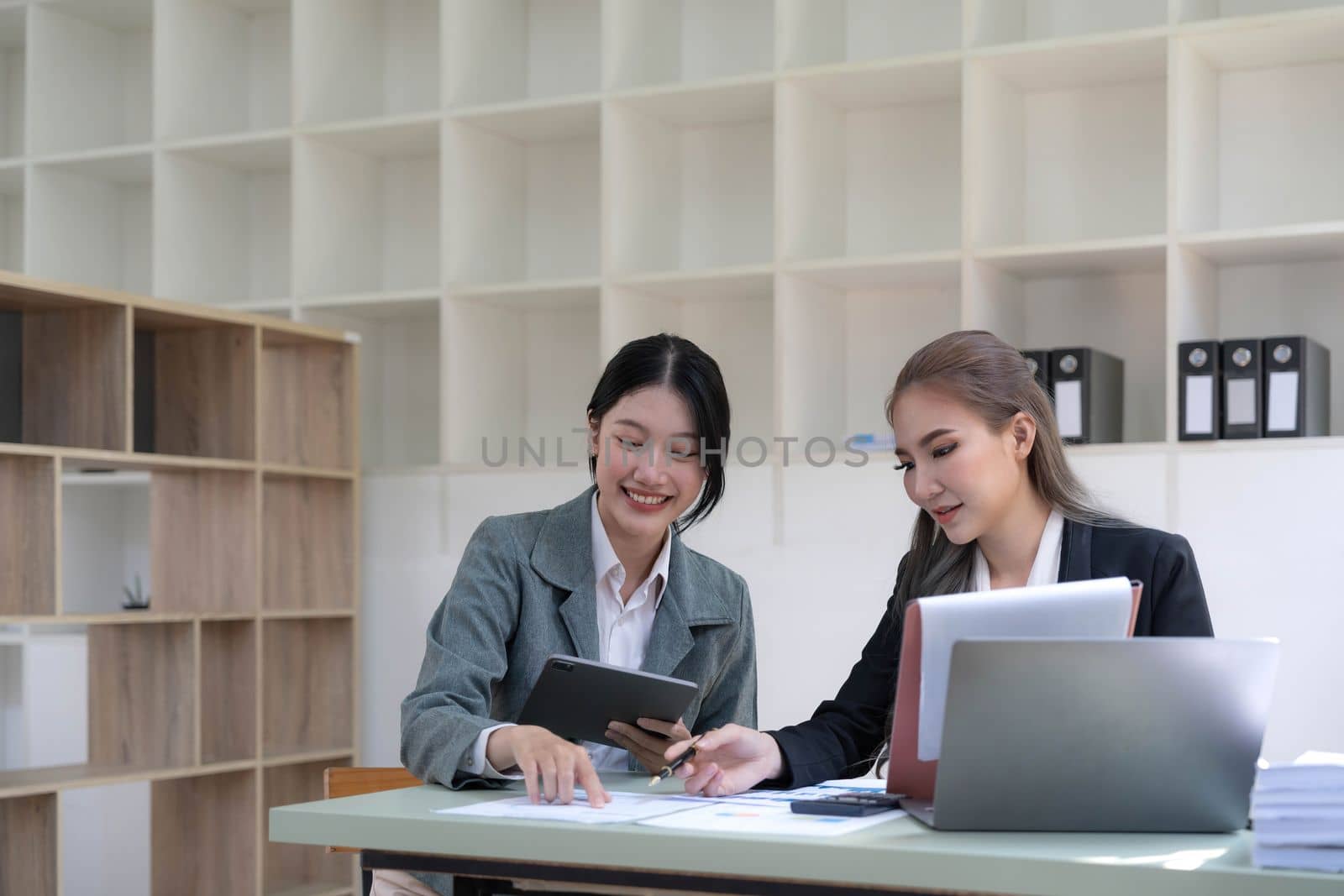 Two young Asian business woman talk, consult, discuss working with new startup project idea presentation analyze plan marketing and investment in the office. by wichayada