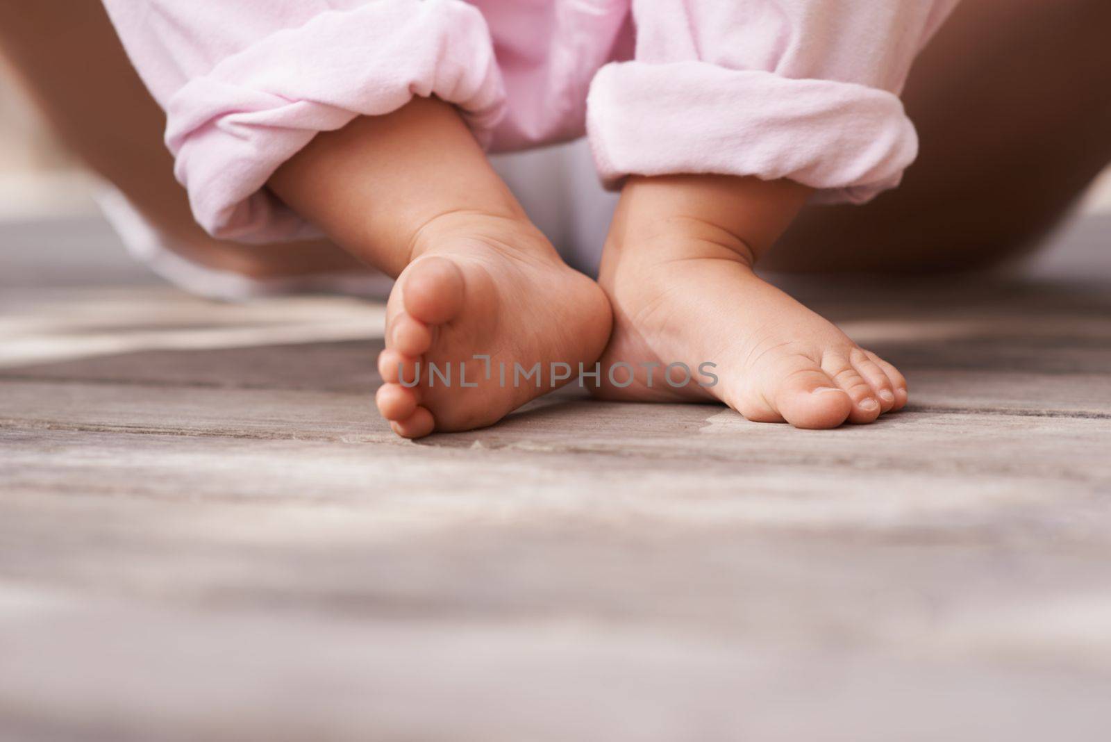 Teeny tiny toes. Closeup image of a babys feet as she sits outside with her mother. by YuriArcurs