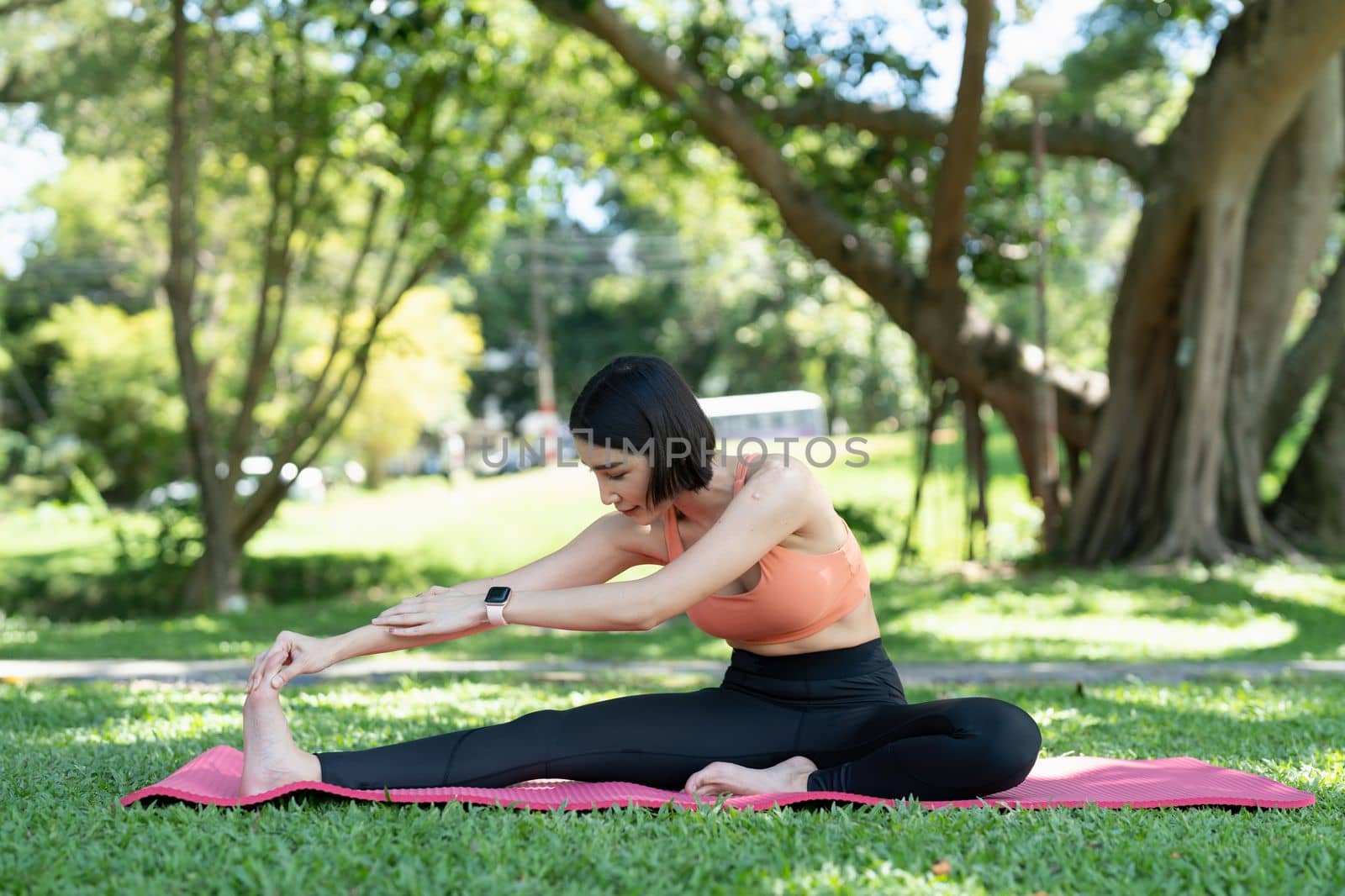 Young attractive girl is doing advanced yoga asana on the fitness mat in the middle of a park. by nateemee