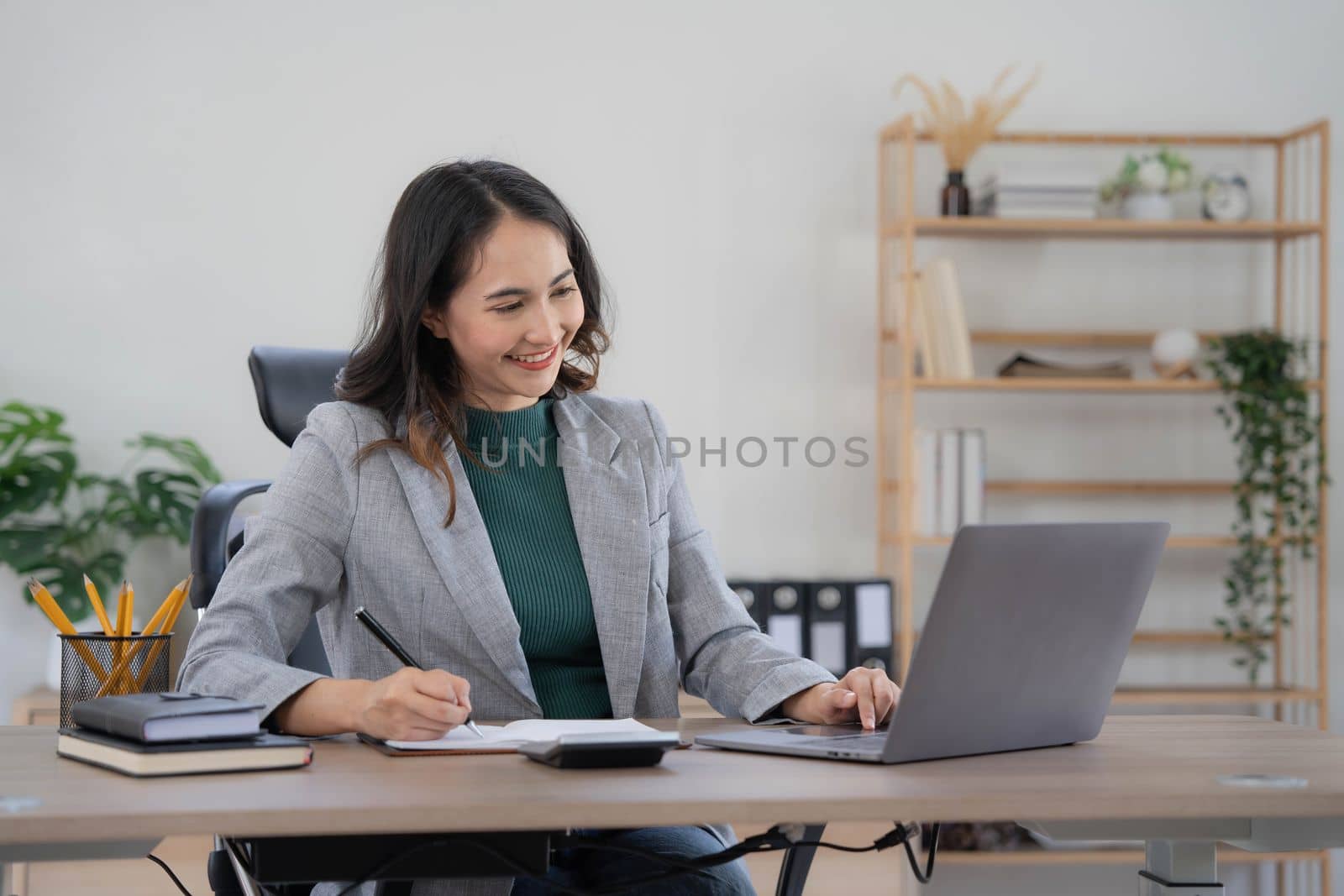 Asian Business woman using calculator and laptop for doing math finance on an office desk, tax, report, accounting, statistics, and analytical research concept..