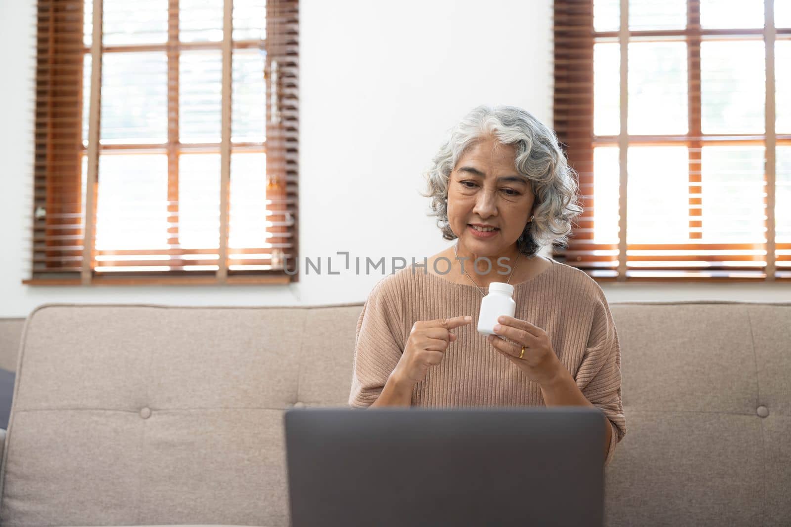 Asian seniors use laptop video conference with doctor about illness and prescription pill in living room at home.Healthy lifestyle.aging at home concept.