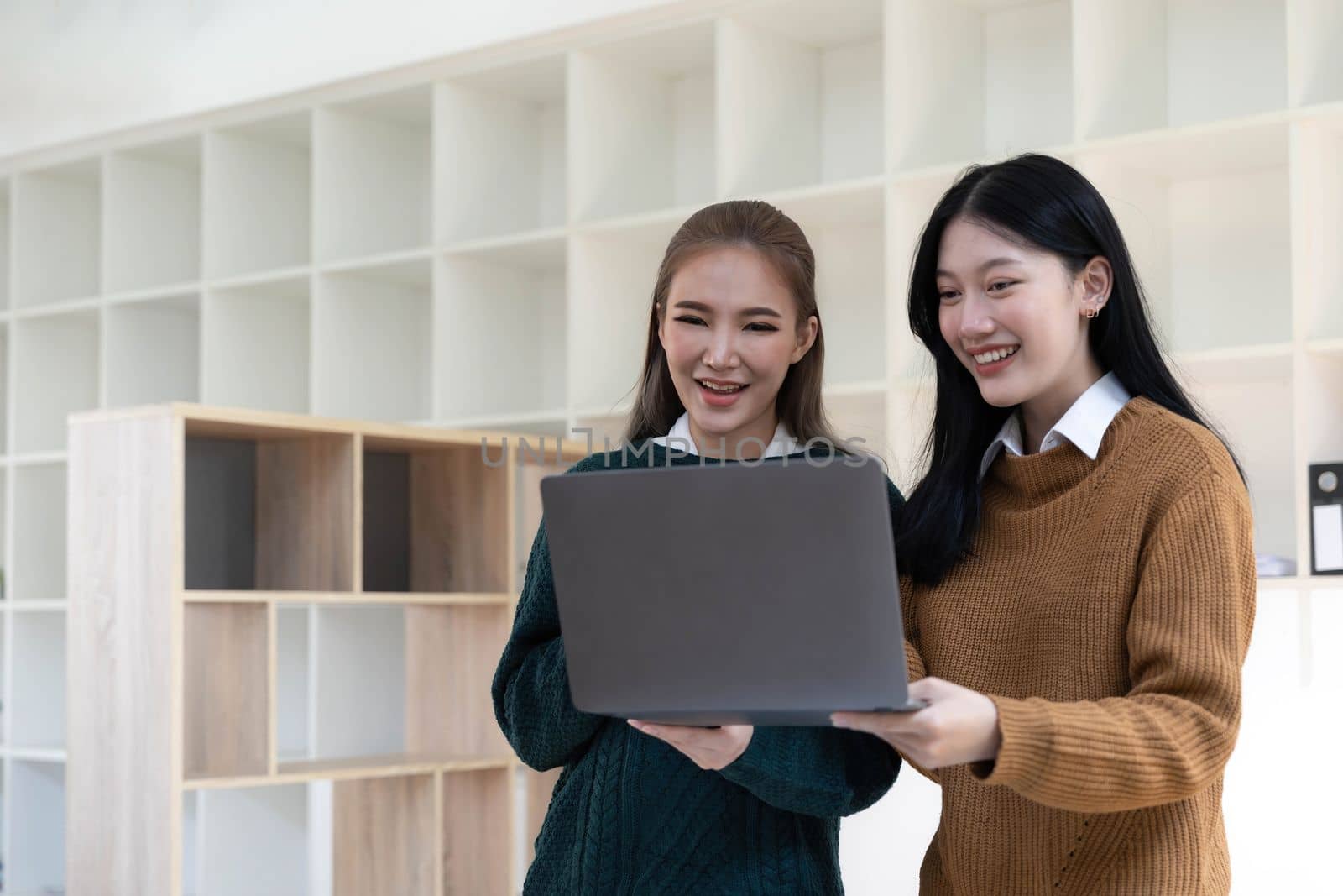 Two beautiful Asian businesswomen standing using digital tablet consulting and analyzing information in office work. by wichayada