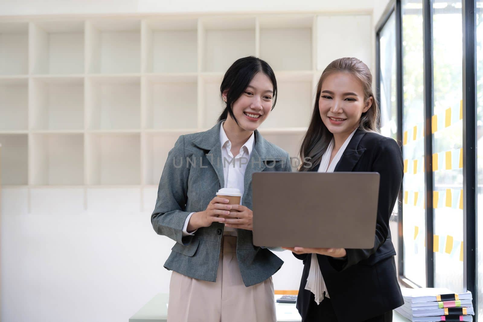 Two beautiful Asian businesswomen standing using digital tablet consulting and analyzing information in office work...