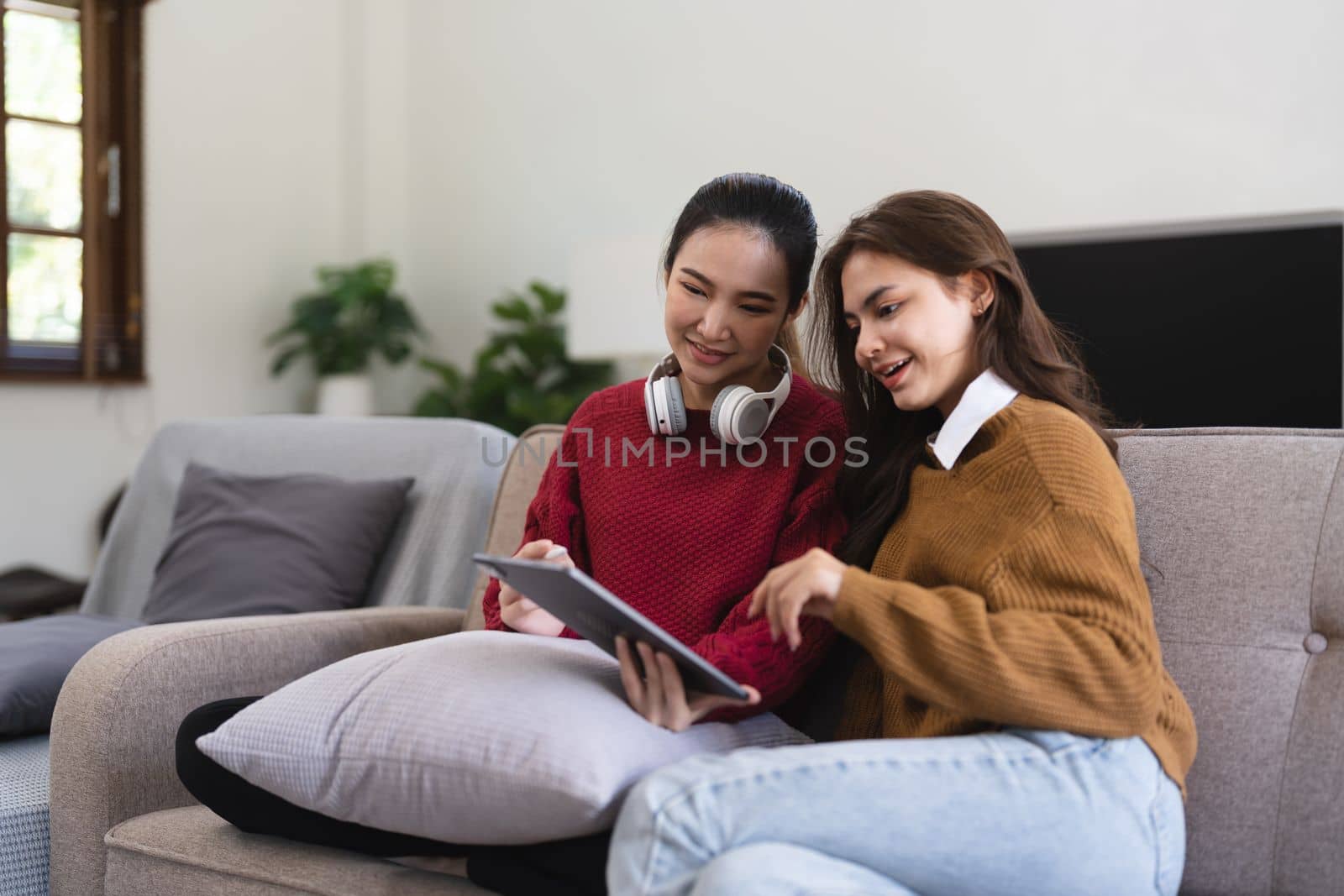 Asian woman friends sitting in living room watching movie on tablet together. Modern female friendship enjoy weekend activity lifestyle with wireless technology at home. by nateemee