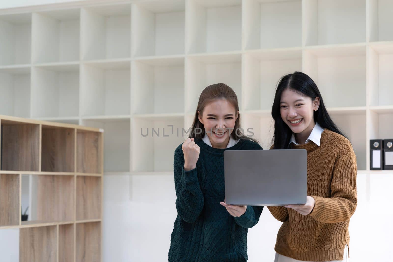 Two beautiful Asian businesswomen standing using digital tablet consulting and analyzing information in office work...