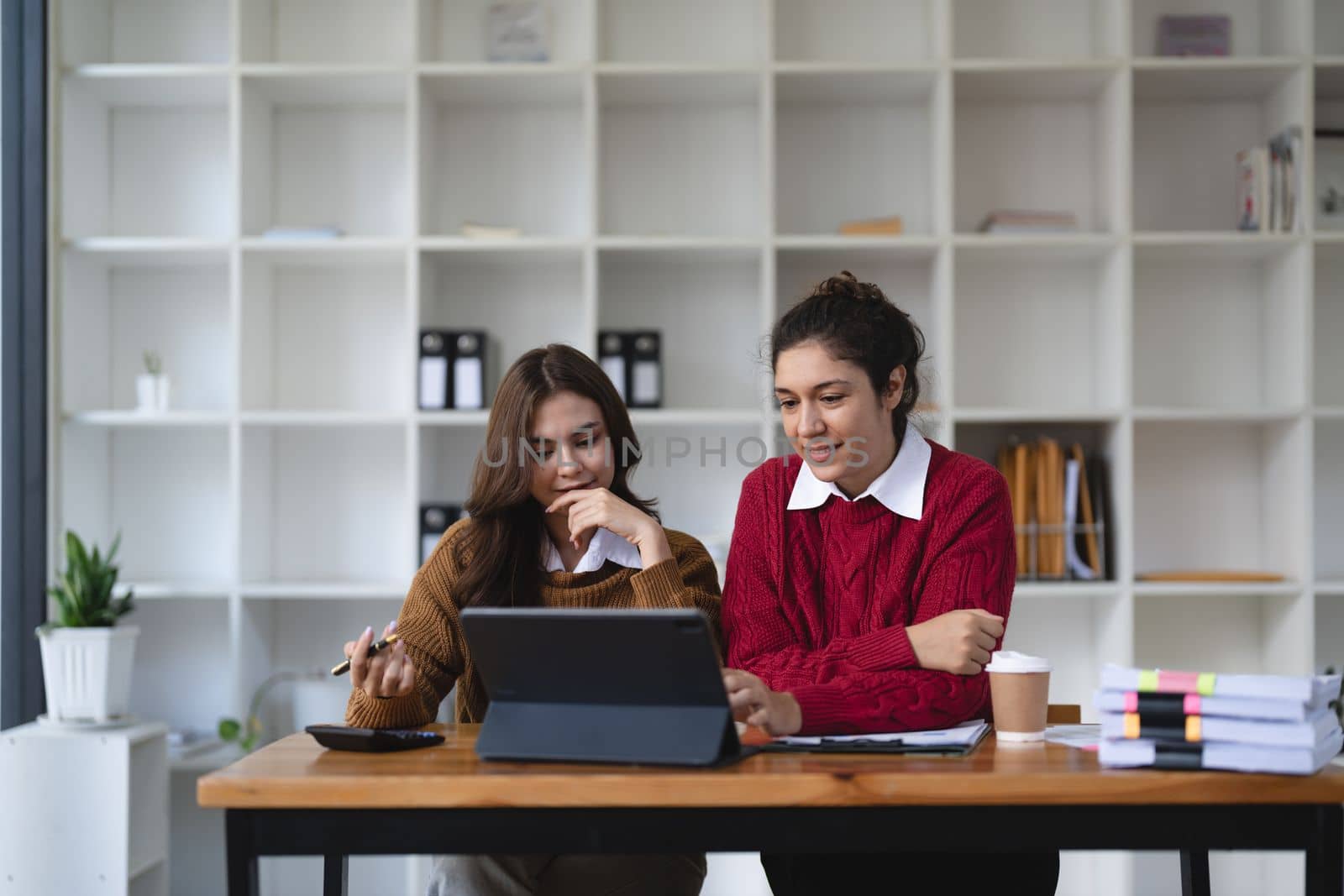 Two multiethnic professionals colleagues working together with laptop and papers in office. Female mentor and young professional sitting in creative office