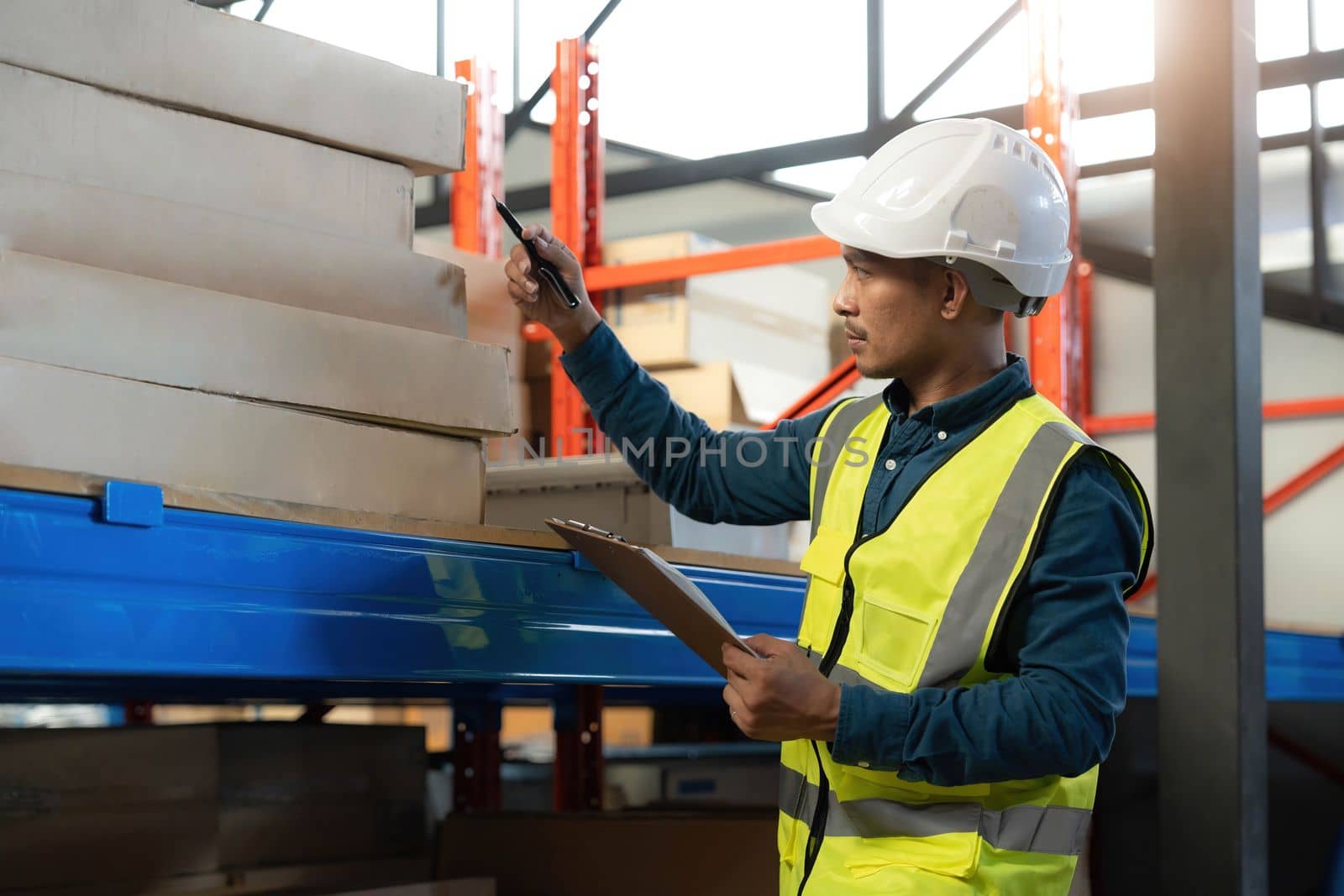 Portrait An Asian warehouse worker in a blue security suit holding clipboard working at store industry. Logistic import export concept Distribution Center. Logistics and export of business