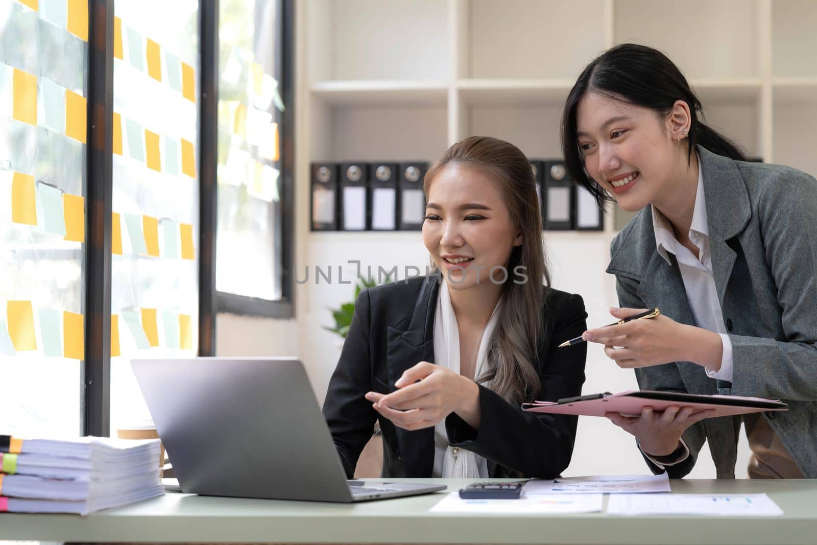 Two young Asian business woman talk, consult, discuss working with new startup project idea presentation analyze plan marketing and investment in the office. by wichayada