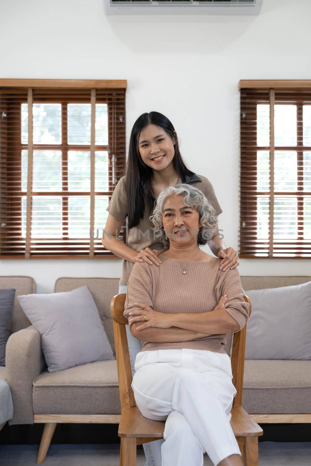 Portrait of Asian lovely family, young daughter hugging older mother. Attractive woman and senior elder mature mom sit on sofa, enjoy activity at home together in living room and smile, look at camera by wichayada