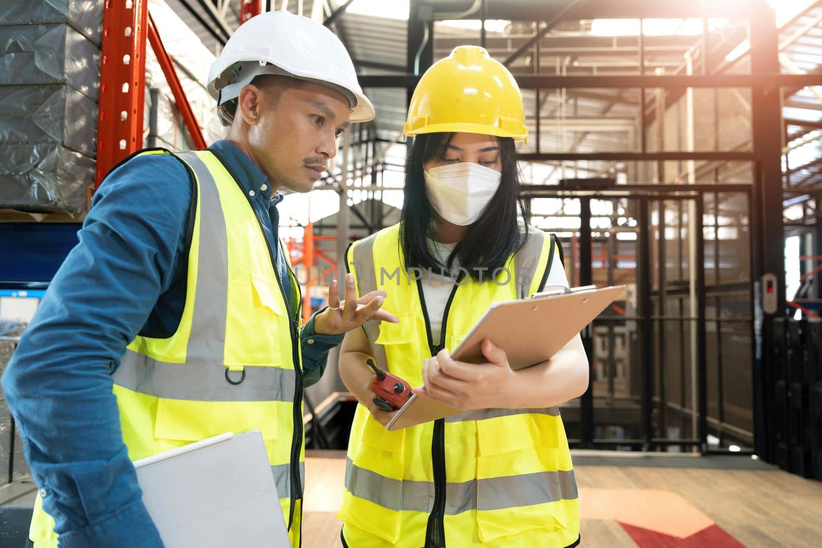 Professional adult Asian male warehouse manager and female worker are working together, checking their inventory in the warehouse or storehouse. by wichayada