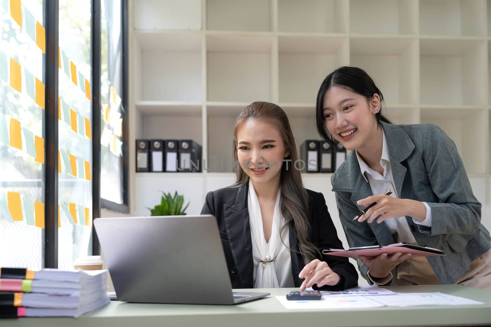 Two young Asian business woman talk, consult, discuss working with new startup project idea presentation analyze plan marketing and investment in the office. by wichayada