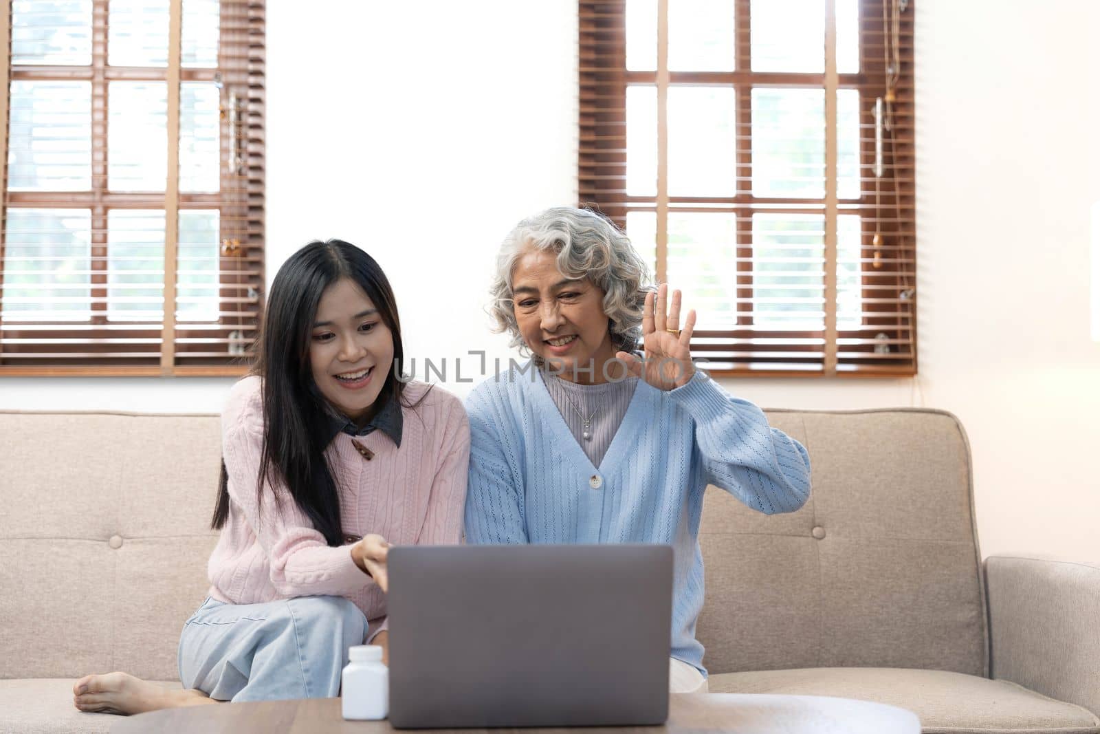 Smiling older mother and adult daughter using phone together, sitting on cozy sofa at home, happy young woman and mature mum looking at smartphone screen, watching video, having fun, two generations..