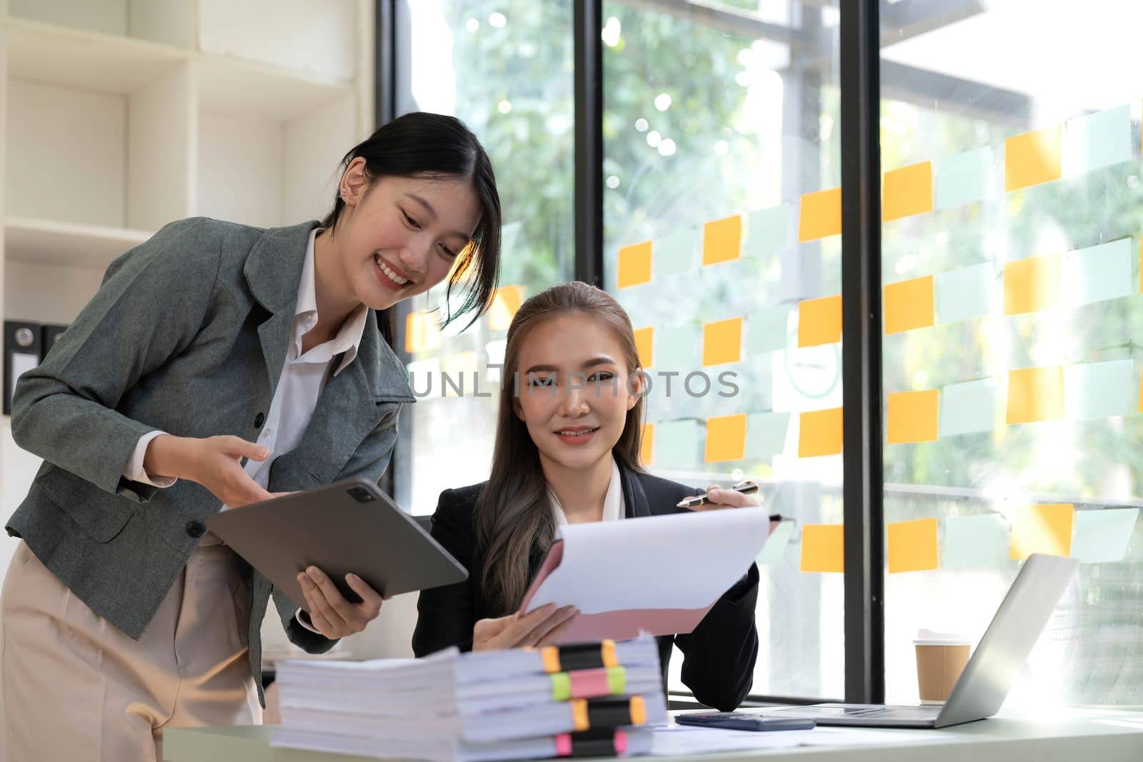 Two young Asian business woman talk, consult, discuss working with new startup project idea presentation analyze plan marketing and investment in the office. by wichayada