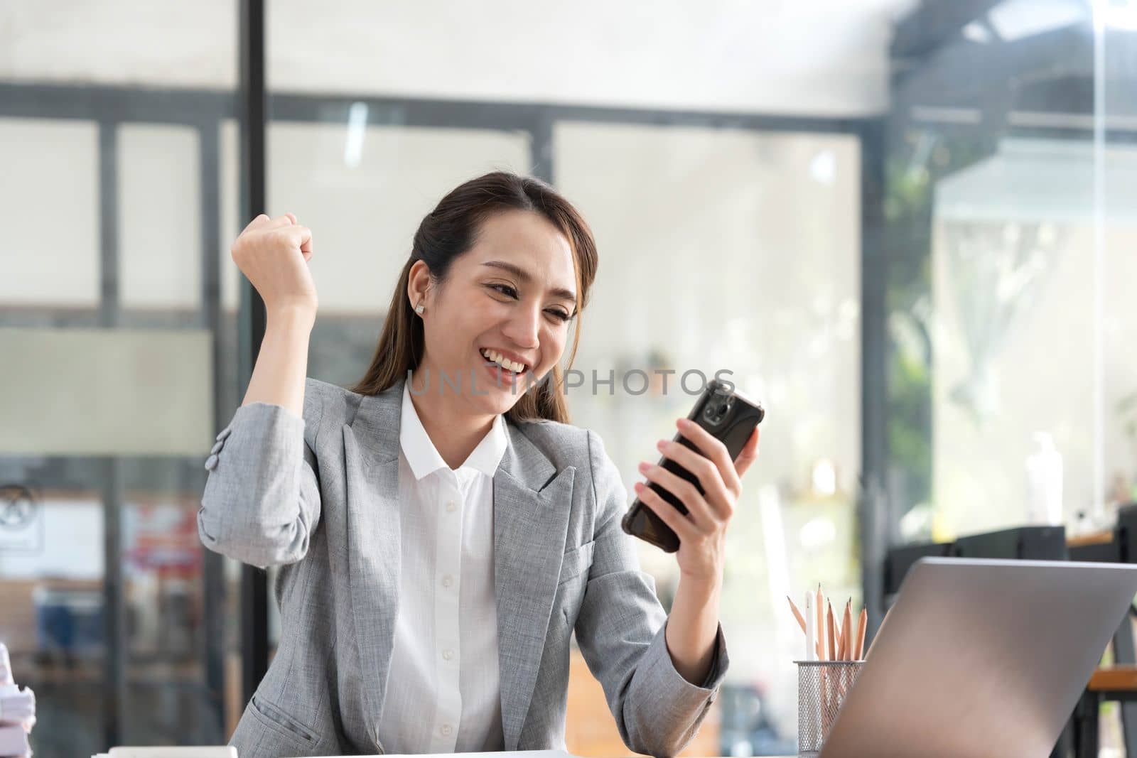 Excited happy Asian woman looking at the phone screen, celebrating an online win, overjoyed young asian female screaming with joy, isolated over a white blur background.