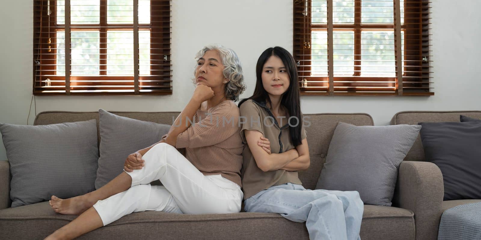 In quarrel elderly mother grown up daughter sit on couch separately having conflict, intergenerational misunderstanding, adult grandchild grandma difficult bad relations different generations concept by wichayada