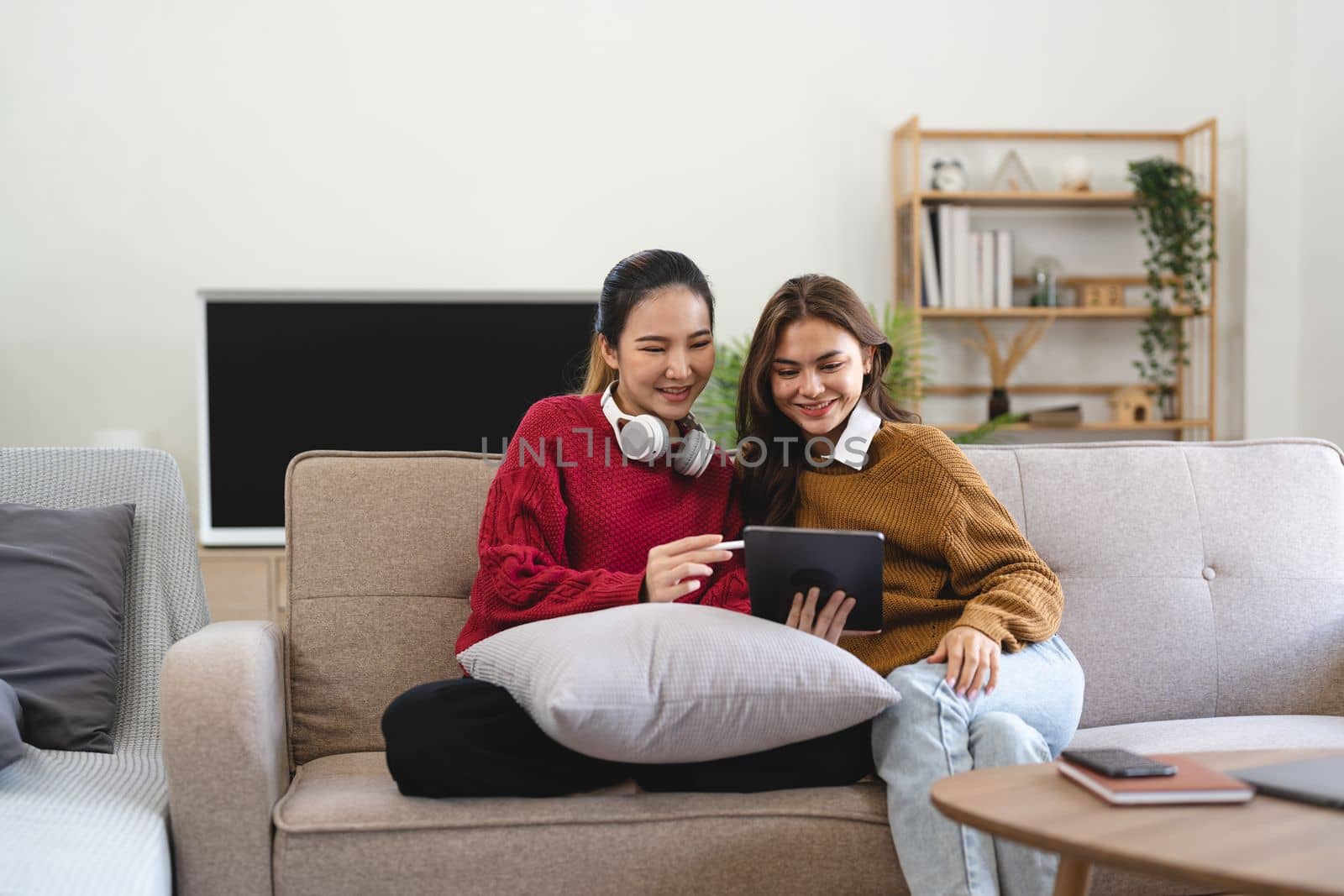 Asian woman friends sitting in living room watching movie on tablet together. Modern female friendship enjoy weekend activity lifestyle with wireless technology at home