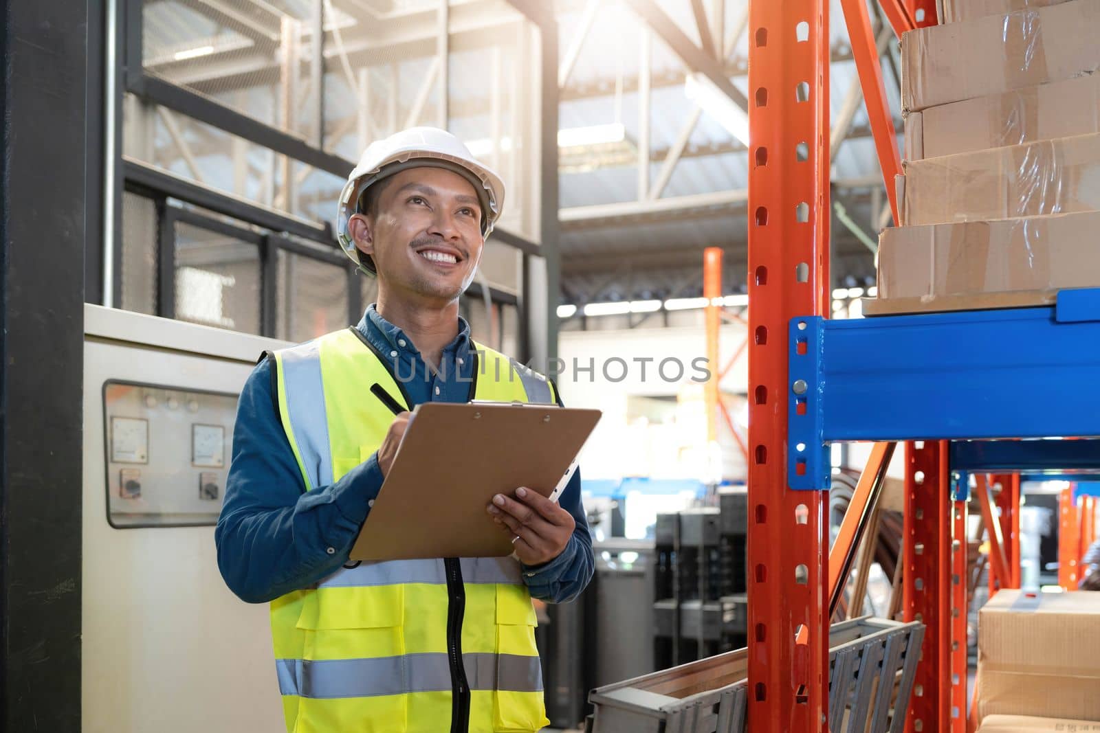 Portrait An Asian warehouse worker in a blue security suit holding clipboard working at store industry. Logistic import export concept Distribution Center. Logistics and export of business. by wichayada