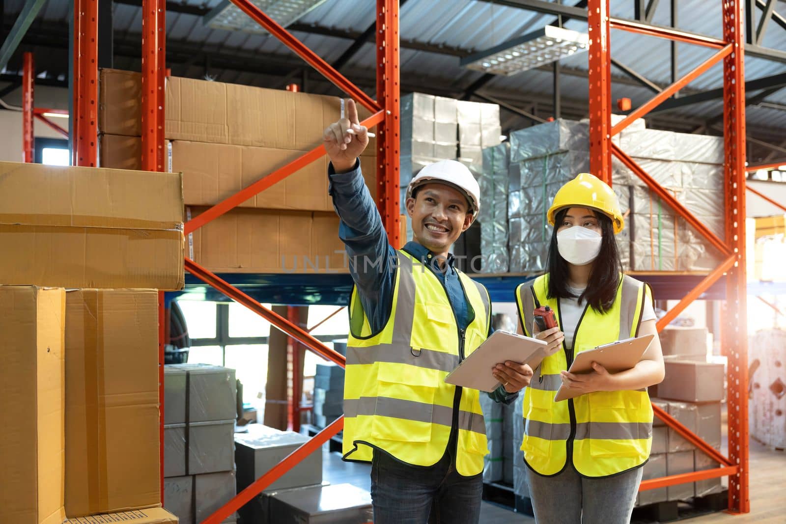 Professional adult Asian male warehouse manager and female worker are working together, checking their inventory in the warehouse or storehouse. by wichayada